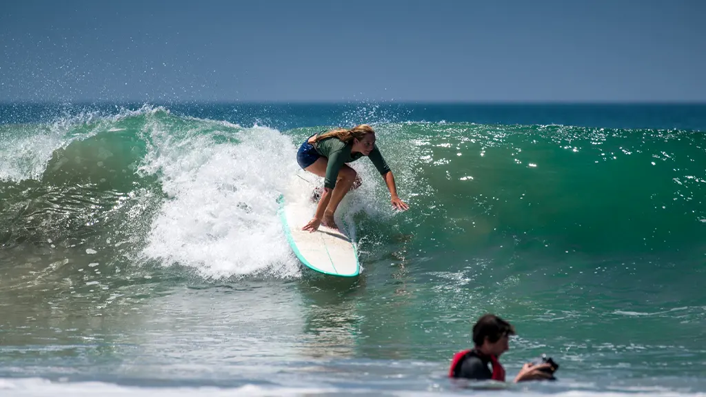 A woman riding a surfboard on a breaking ocean wave in Hikkaduwa, Sri Lanka.