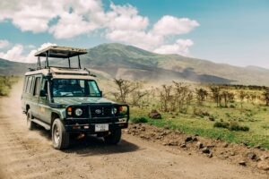 Une jeep de safari verte soulevant de la poussière sur une piste en terre devant un paysage montagneux au Sri Lanka.