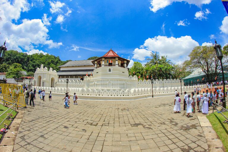 Vue panoramique du Temple de la Dent sacrée à Kandy avec des visiteurs habillés en blanc sous un ciel bleu ensoleillé au Sri Lanka.