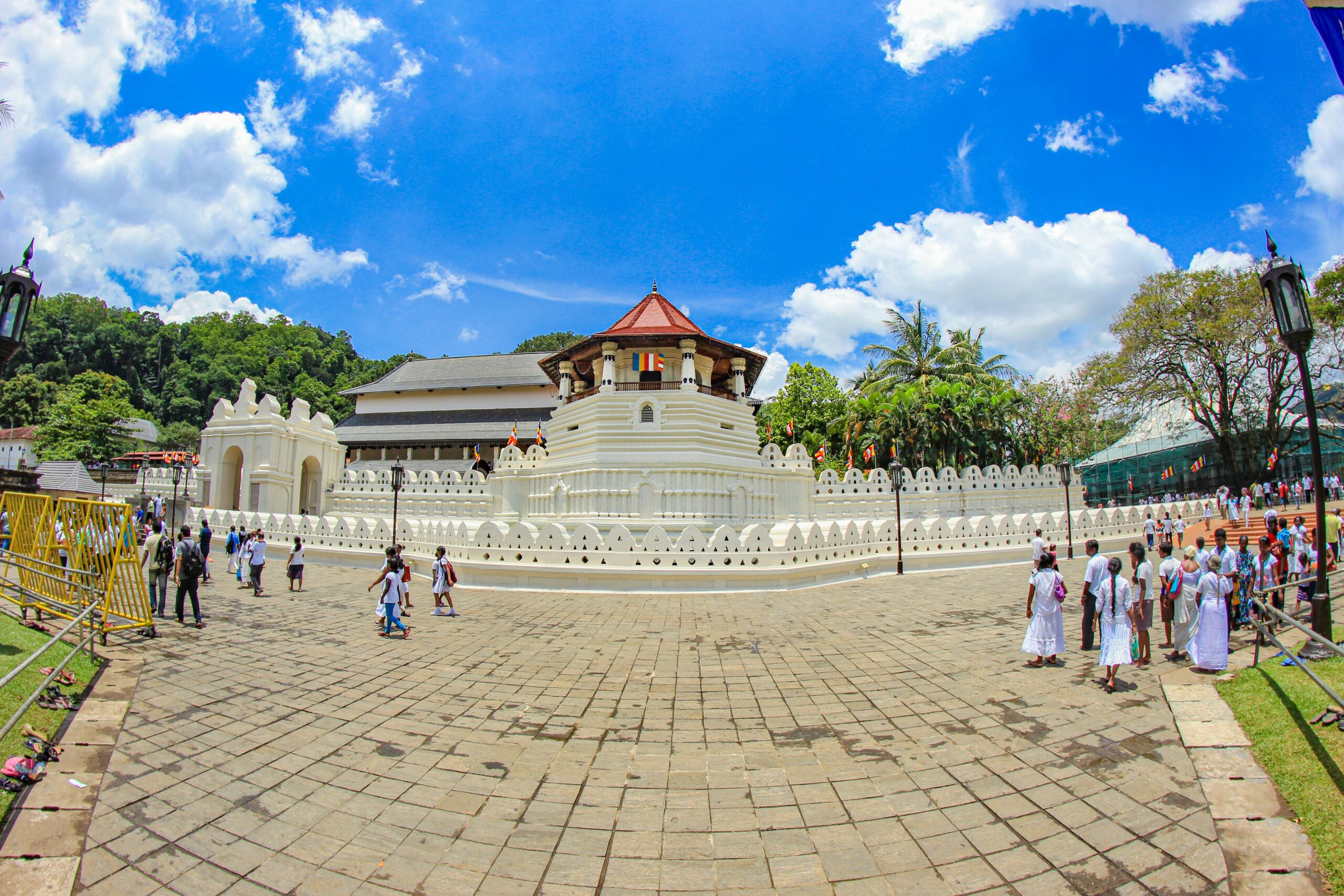 Vue panoramique du Temple de la Dent sacrée à Kandy avec des visiteurs habillés en blanc sous un ciel bleu ensoleillé au Sri Lanka.