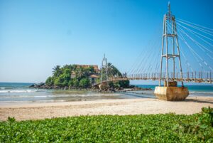 Tropischer Strand auf Sri Lanka mit türkisblauem Meer, hellem Sand und hohen Palmen bei sonnigem Wetter.