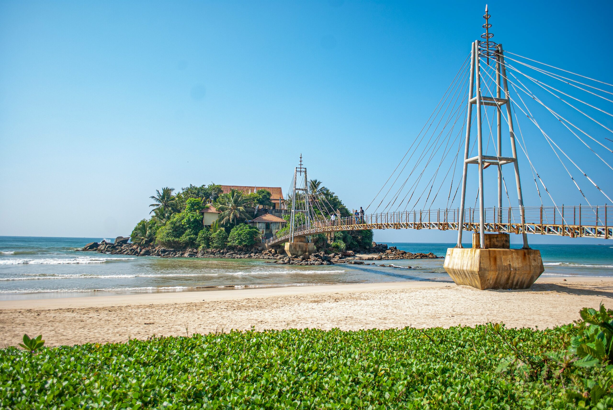 Tropischer Strand auf Sri Lanka mit türkisblauem Meer, hellem Sand und hohen Palmen bei sonnigem Wetter.